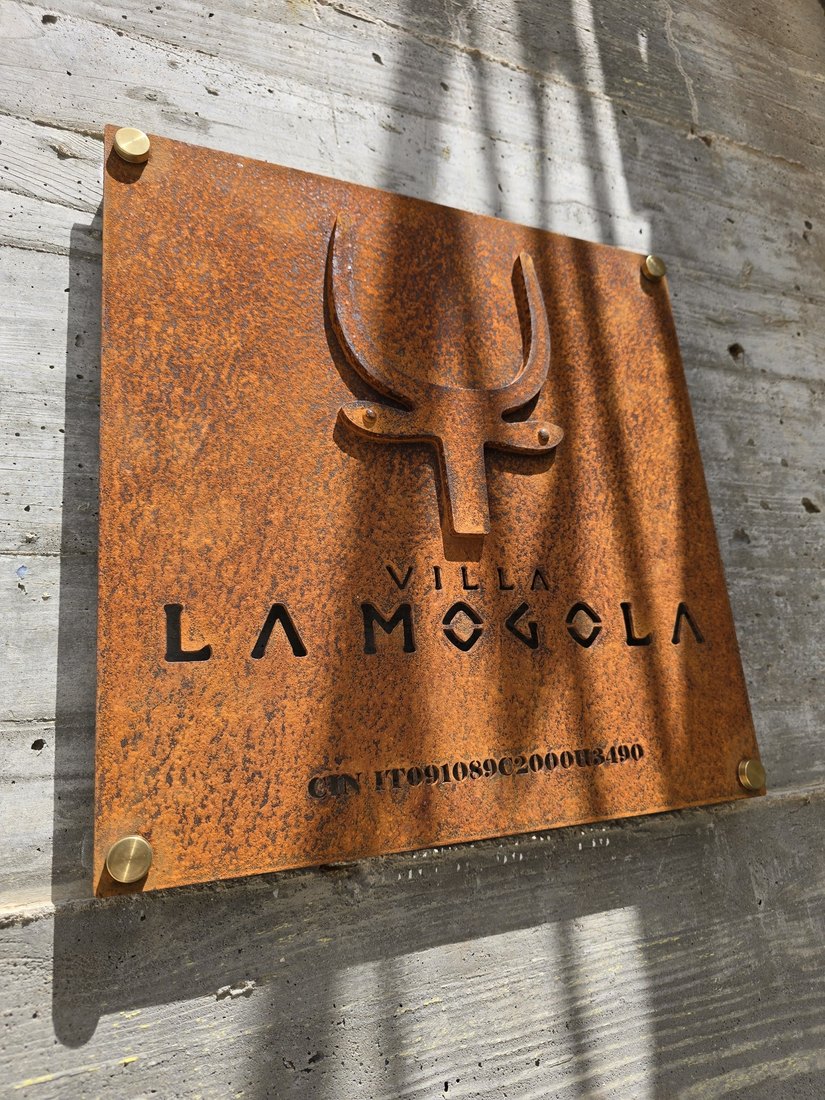 Targa in CorTen con logo e nome traforati, fissata al muro con distanziali in ottone
