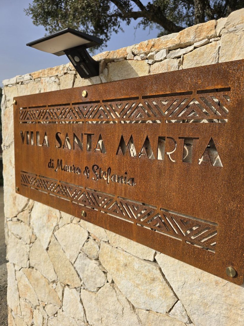Insegna lunga in CorTen con decori geometrici traforati, su un muro in pietra