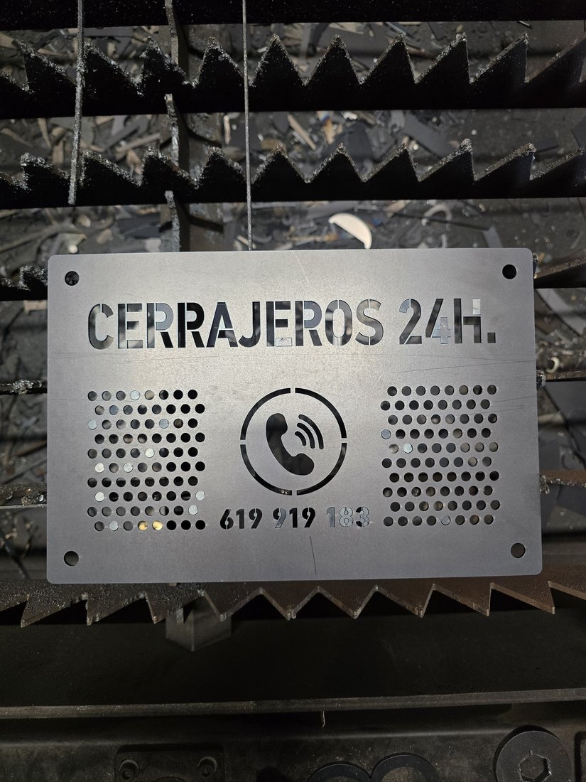 Targa in CorTen grigia con icona del telefono e griglie di fori, sul banco del LASER