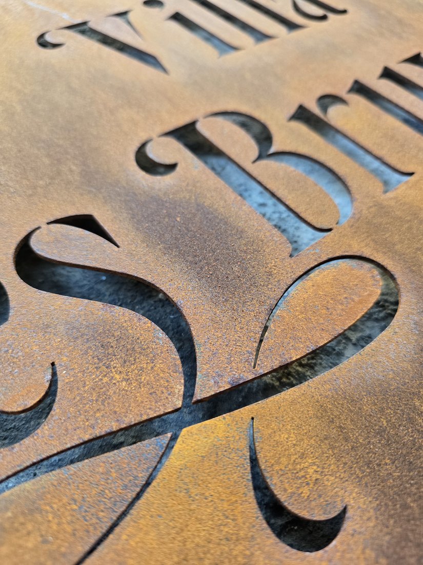 Lettere corsive traforate nel CorTen arrugginito, da vicino
